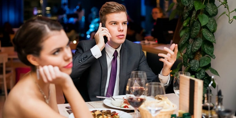 Man talking on a cell phone while on a date with his girlfriend 