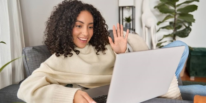 Latin happy smiling curly young woman sitting on couch using laptop 