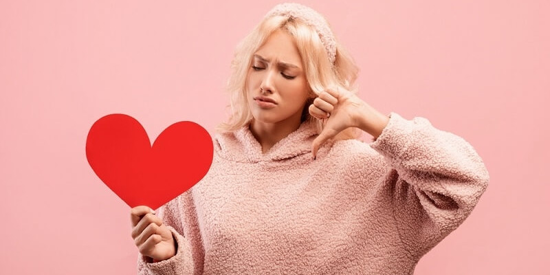 women feeling bad and showing thumbs down while holding heart shape card in her hand