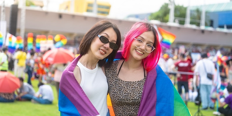 Happy young asian lesbian couple with pride movement LGBT wrapped in rainbow flag for freedom.