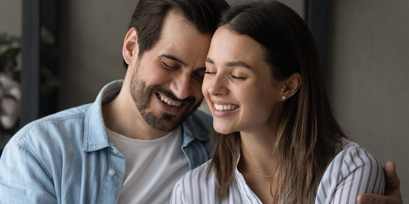Couple in love embracing sit together on sofa. Loving handsome husband touch foreheads with beloved wife, feeling bond enjoy tender moment.